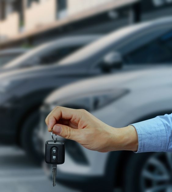 Person holding a car key with a blurred parking lot full of cars in the background