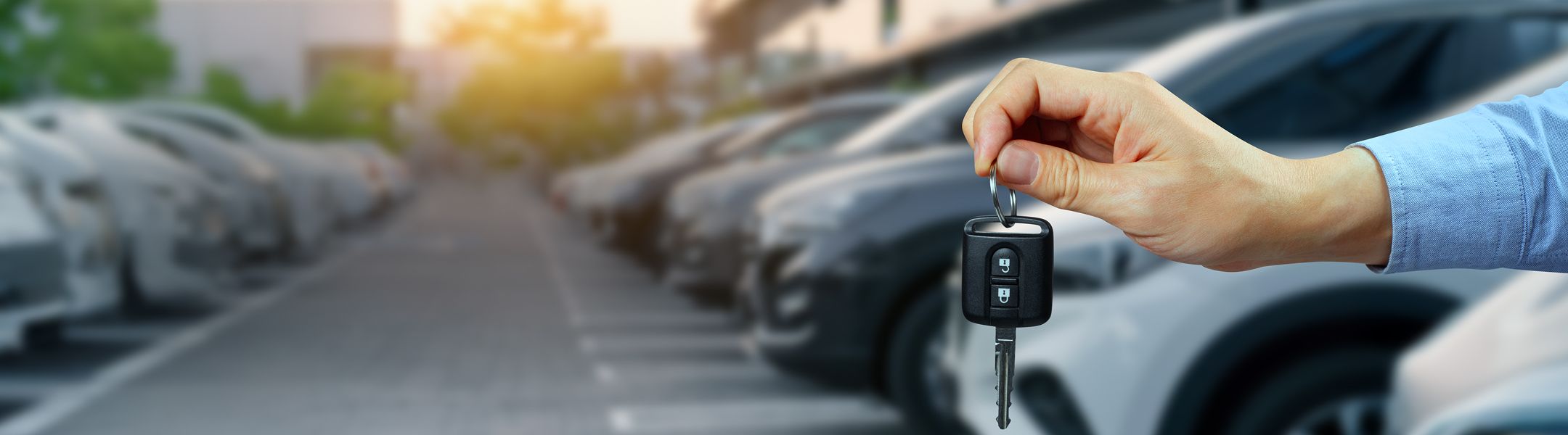 Person holding a car key with a blurred parking lot full of cars in the background